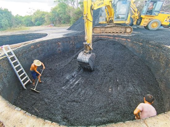 日前，在海口马禄村附近一椰壳露天烧炭黑加工点，烧炭灶内的工人在配合挖掘机挖炭。