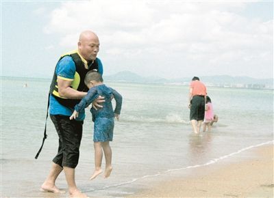 林启辉将海边玩耍摔跤的孩子抱到沙滩上。三亚日报记者汪慧珊摄